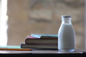 A glass of milk sitting on a table with books and a pencil on a table.