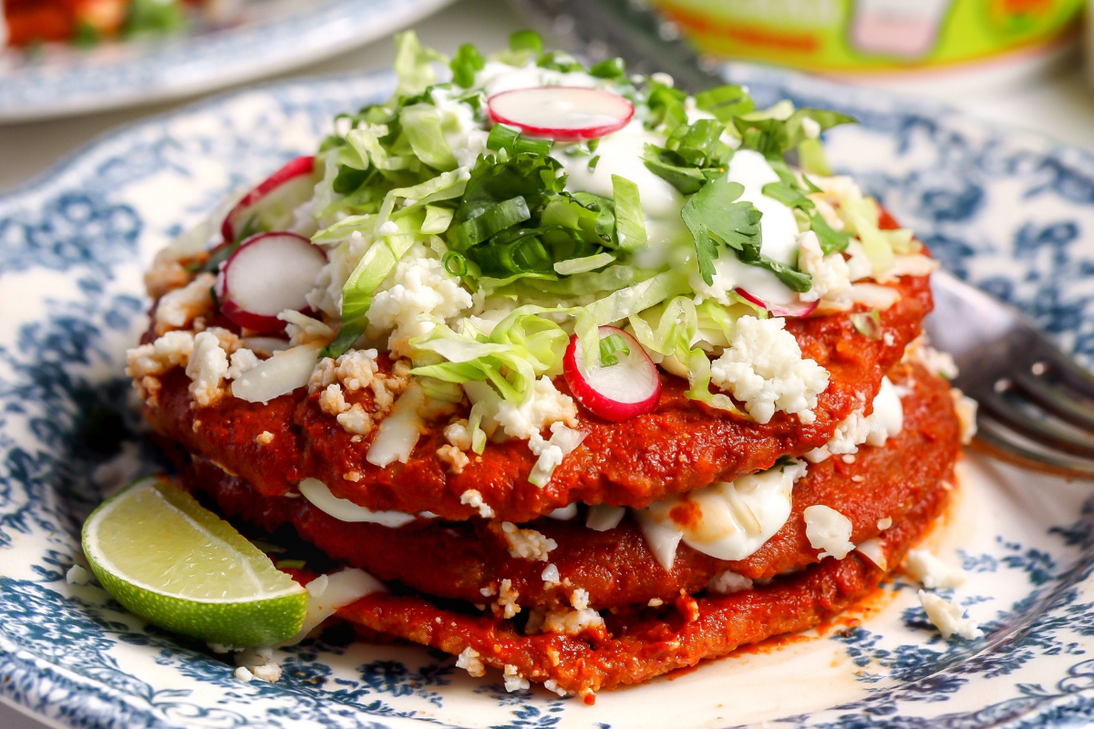 A stack of Sonoran enchiladas topped with sour cream, cheese, lettuce and radishes